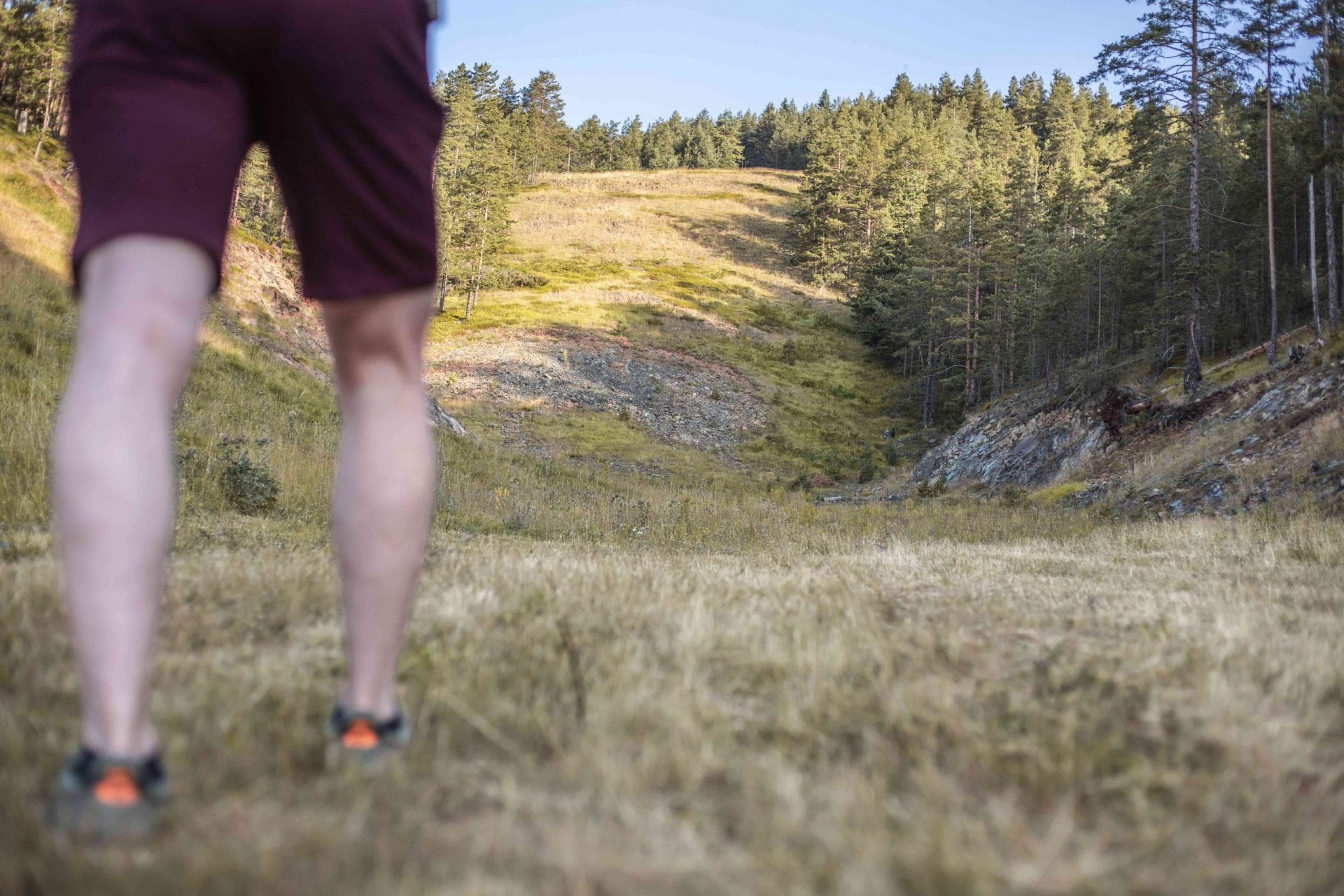 un chico en pantalón corto se prepara para subir una pendiente pronunciada en una colina boscosa y rocosa