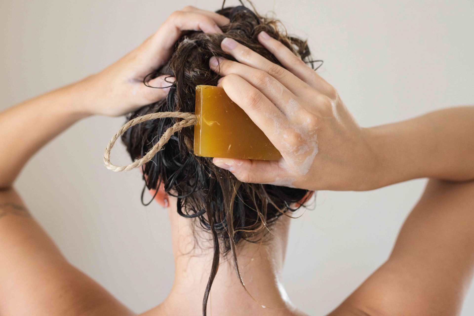 parte trasera de la cabeza de una mujer lavándose el pelo con una barra de champú marrón