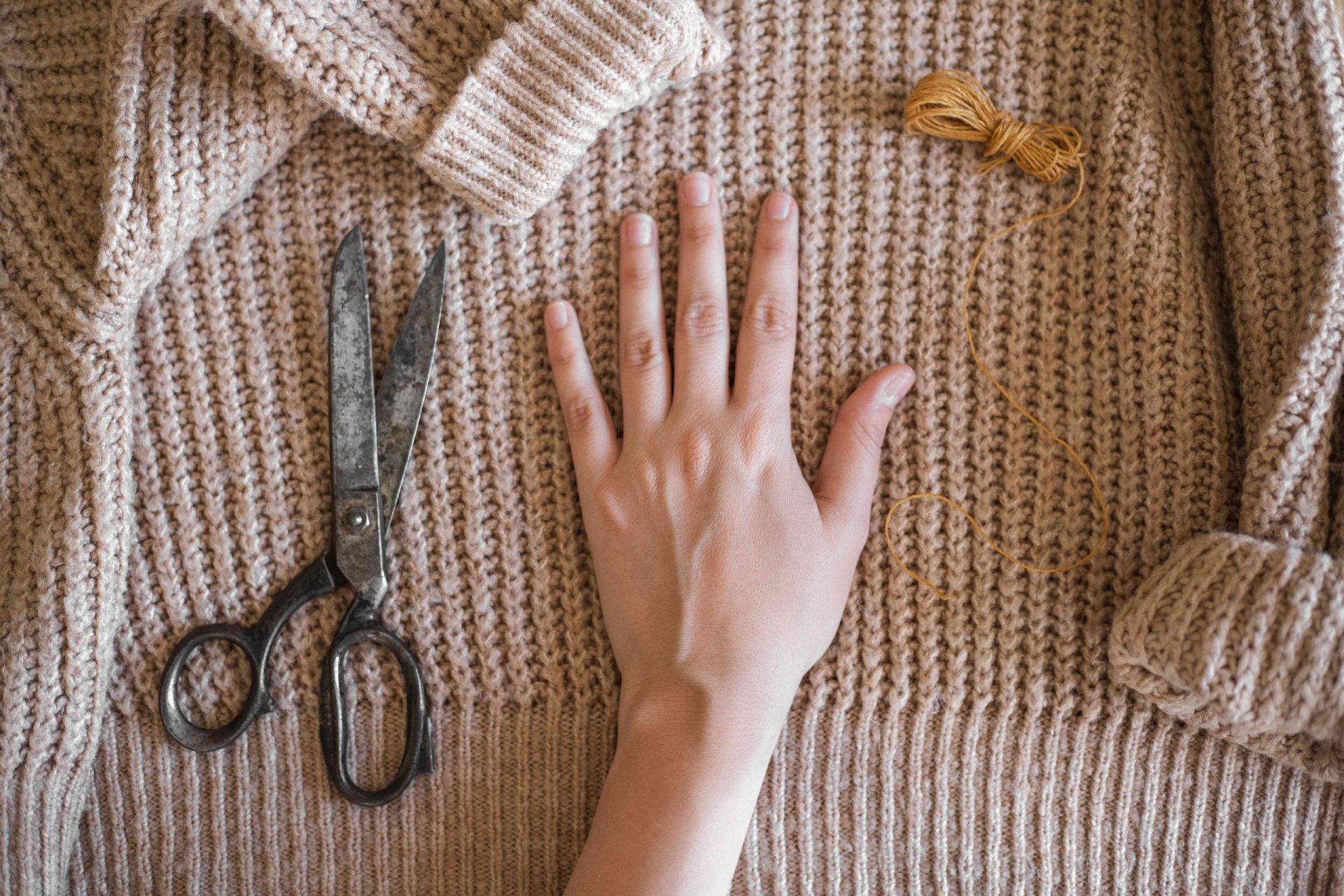 la mano se extiende sobre un jersey grueso de color canela para medirlo con tijeras e hilo