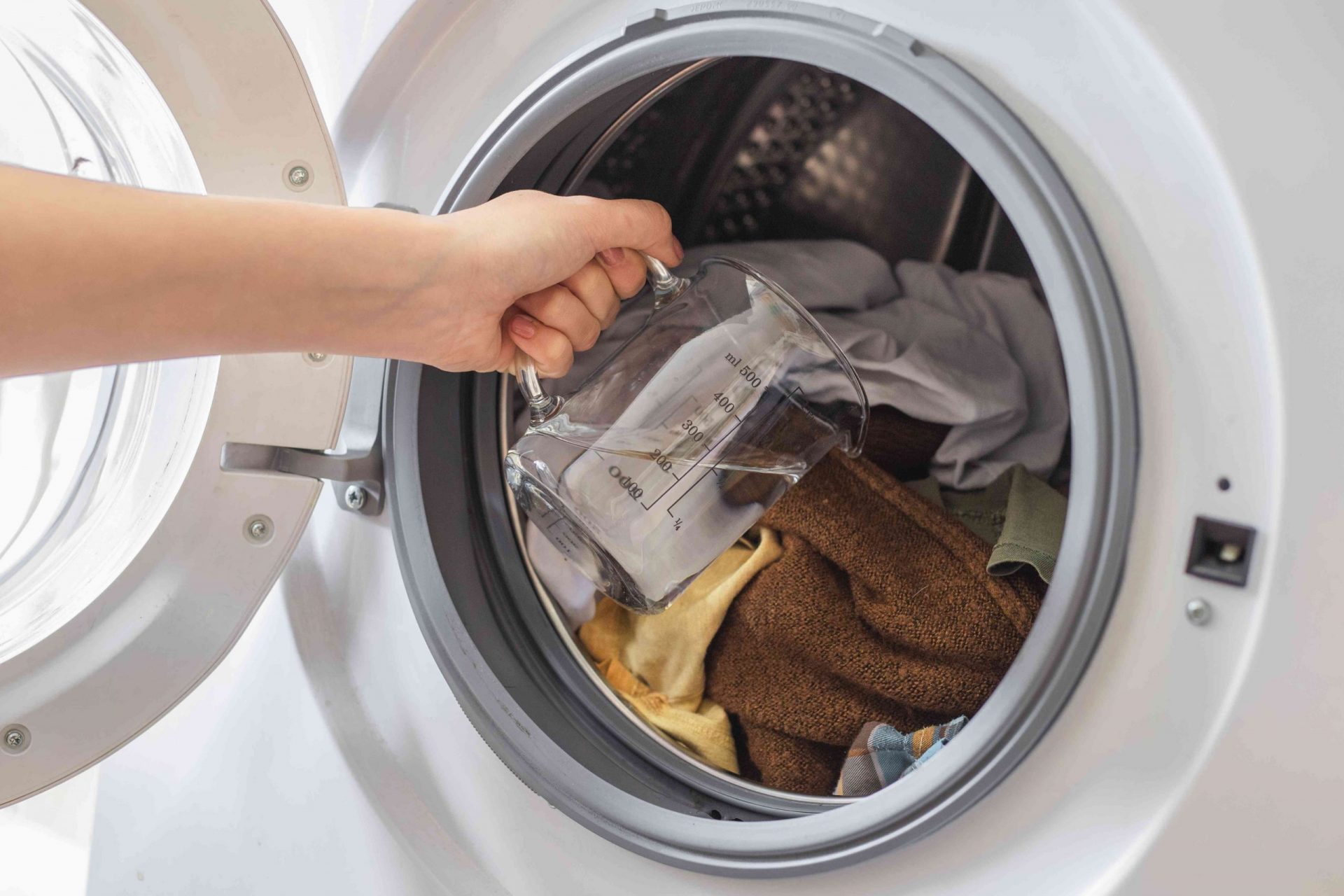 la mano vierte vinagre directamente sobre la ropa sucia de la lavadora abierta