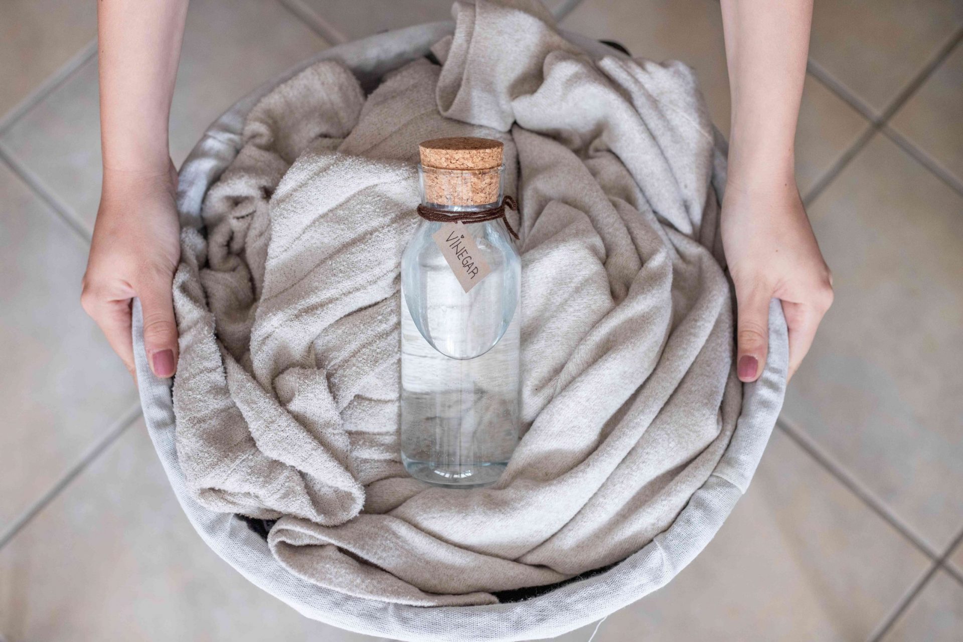 toma aérea de unas manos sosteniendo una cesta de mantas de marfil con una botella de vidrio de vinagre blanco