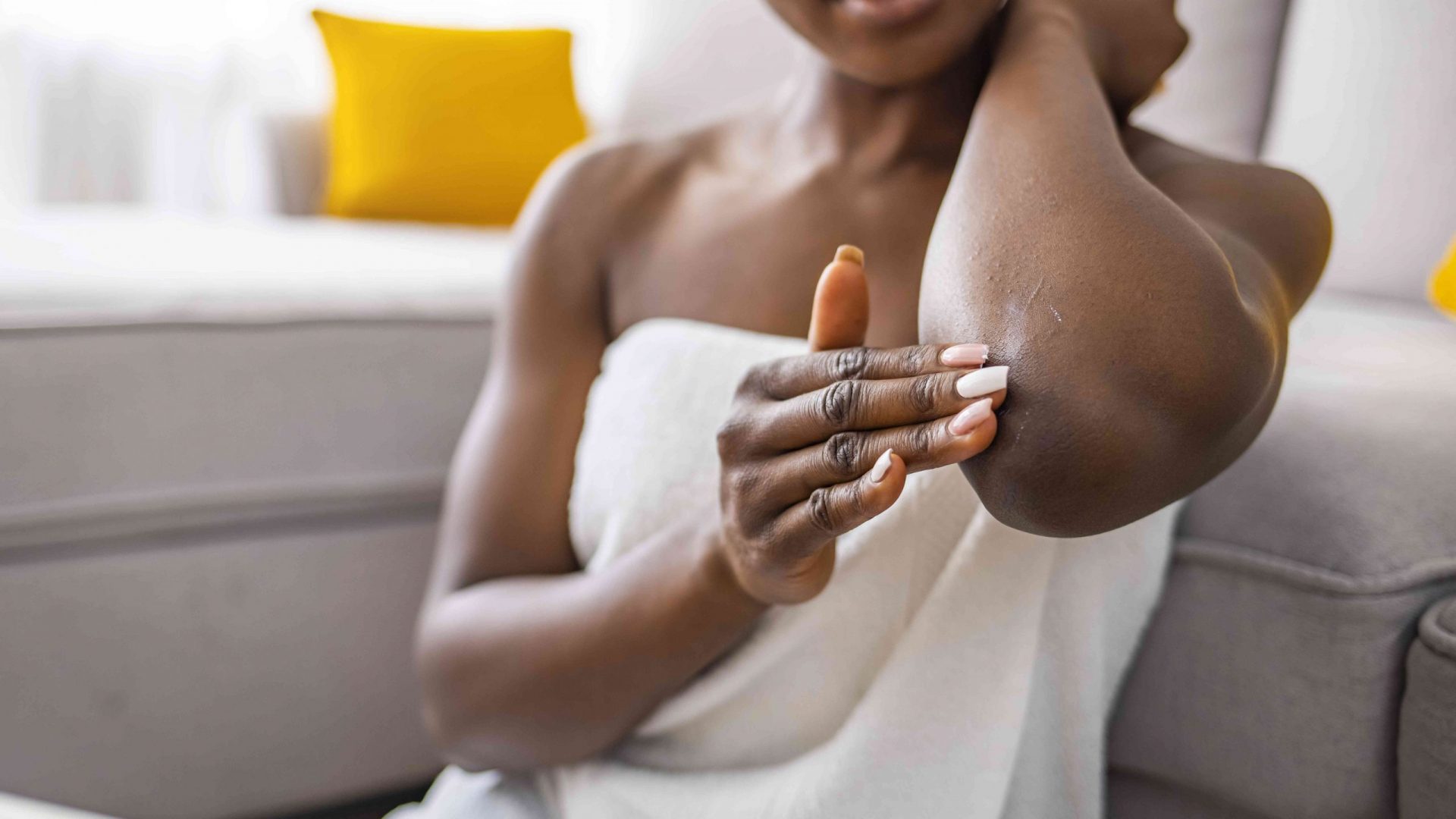 Mujer sentada en el sofá del salón sosteniendo un pequeño tubo con suero que cuida la salud de la belleza de la piel aplica una crema ultra-suavizante en la zona de los codos
