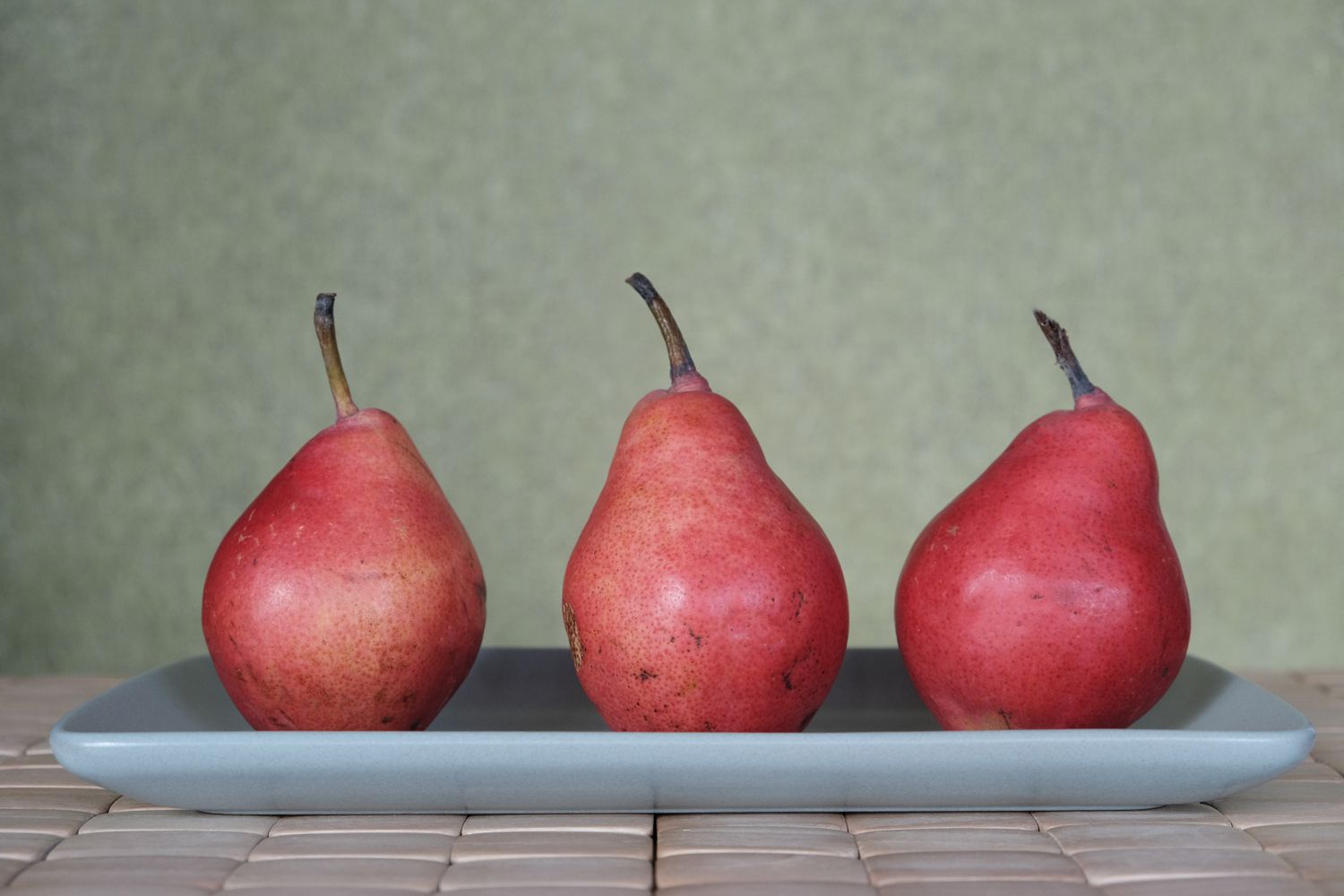 tres peras rojas de Anjou sentadas en posición vertical en una bandeja gris
