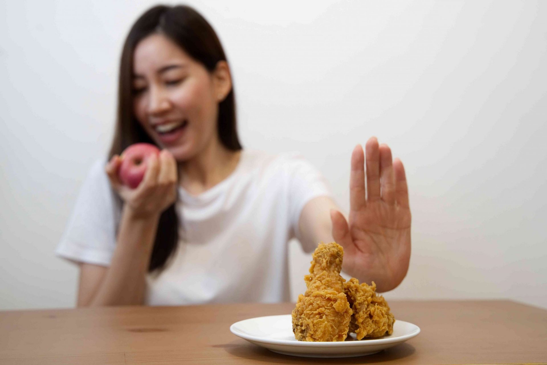 Chica joven a dieta por concepto de buena salud. Primer plano de una mujer que rechaza la comida basura empujando su pollo frito favorito y elige manzana roja y ensalada para gozar de buena salud.